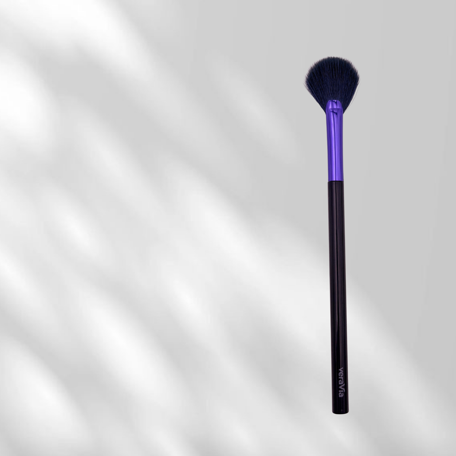 Makeup brush with purple ferrule and black handle on a gradient gray background