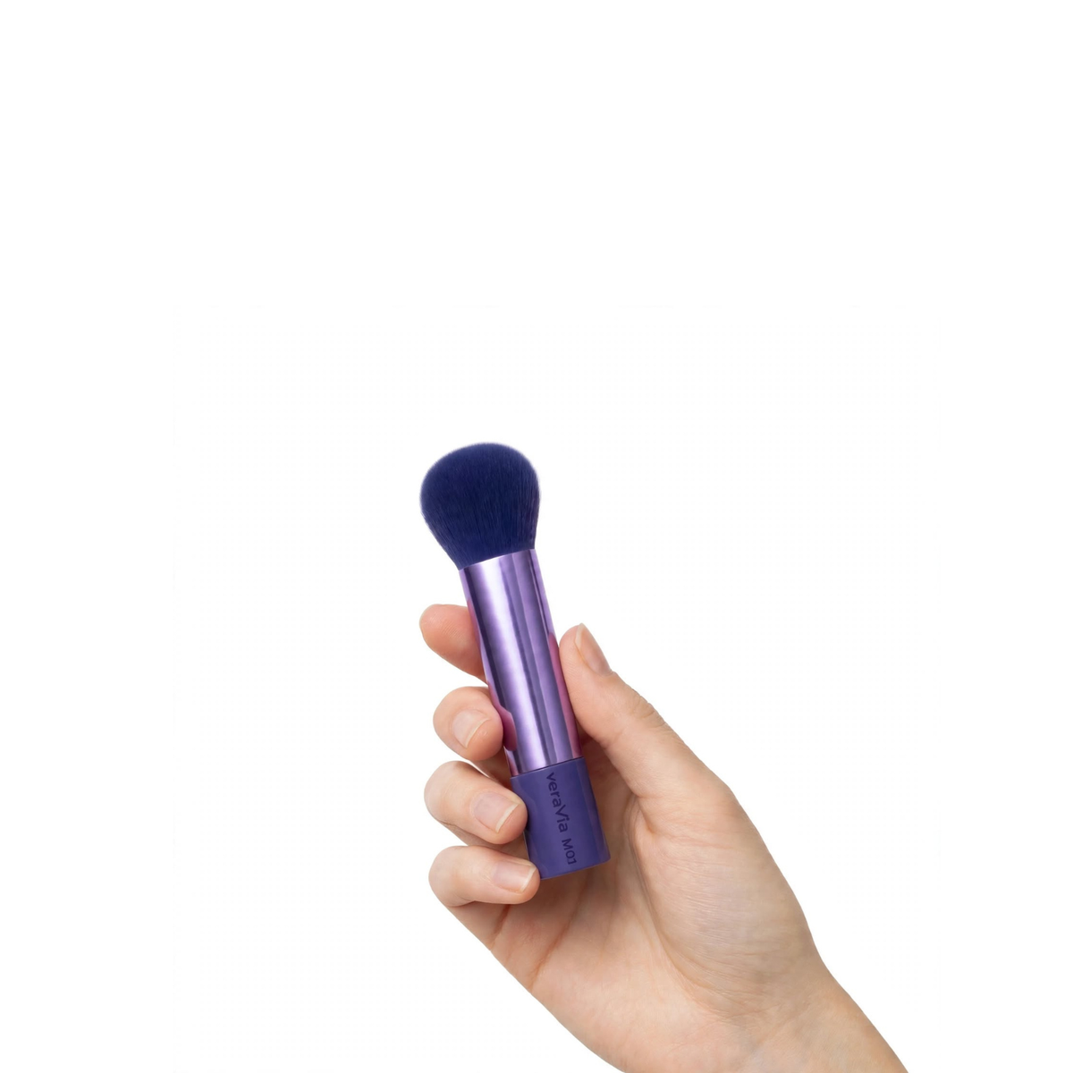 Hand holding a compact veraVia M01 brush with a spherical navy bristle ball head and short purple metallic handle, showing the brush fits within one hand palm, on white background